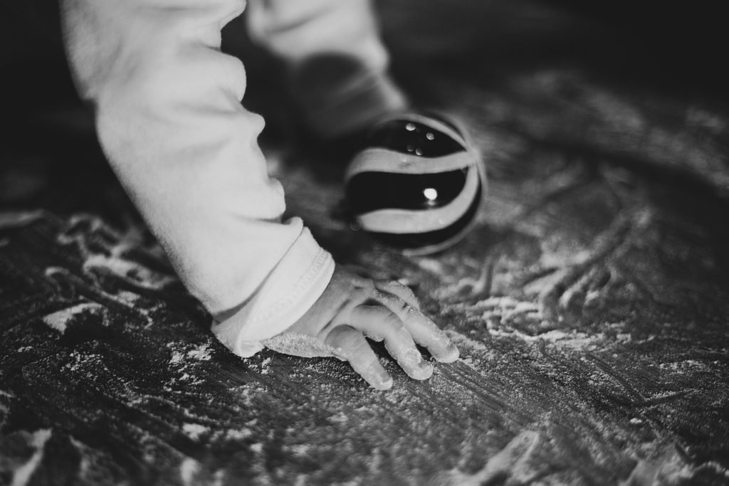 In bianco e nero, una manina appoggiata sulla farina accanto a una pallina di Natale a strisce