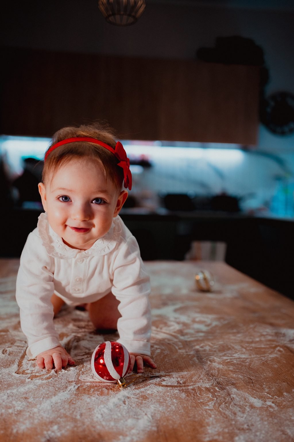 La bimba col fiocco rosso gattona verso l’obiettivo, con una pallina di Natale a strisce davanti
