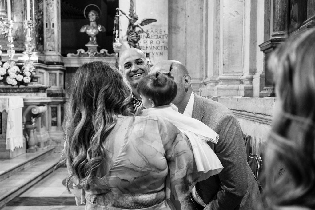 In bianco e nero, davanti all’altare barocco, genitori e parenti si stringono attorno alla bimba