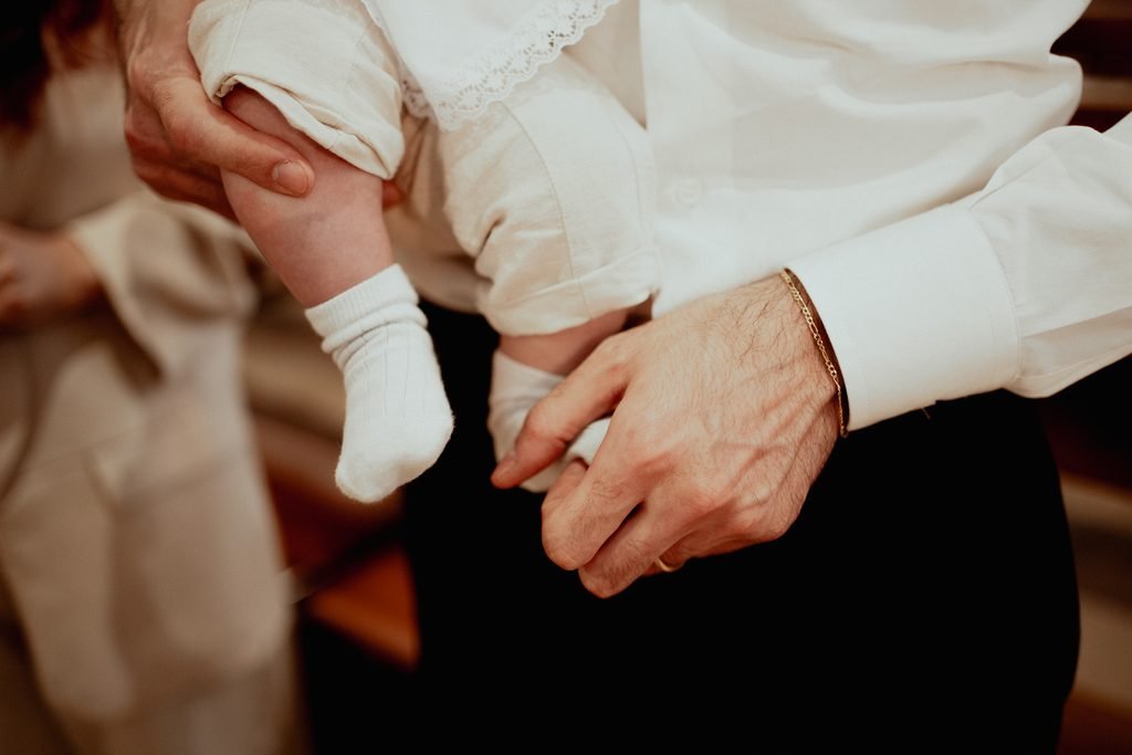 Un calzino bianco e la mano di un uomo con la fede che sostiene il bimbo in braccio