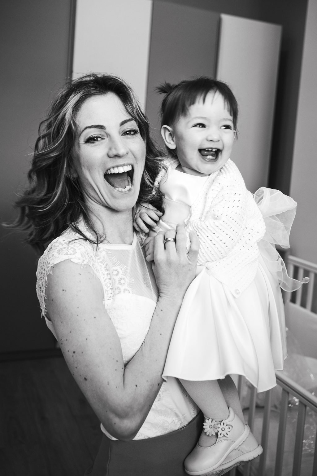 In bianco e nero, la mamma solleva la bimba vestita di bianco e ridono tutte e due