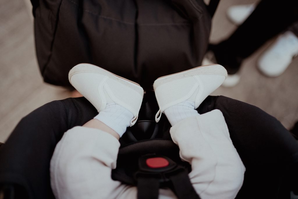 Le scarpine bianche del bimbo spuntano dal passeggino nero