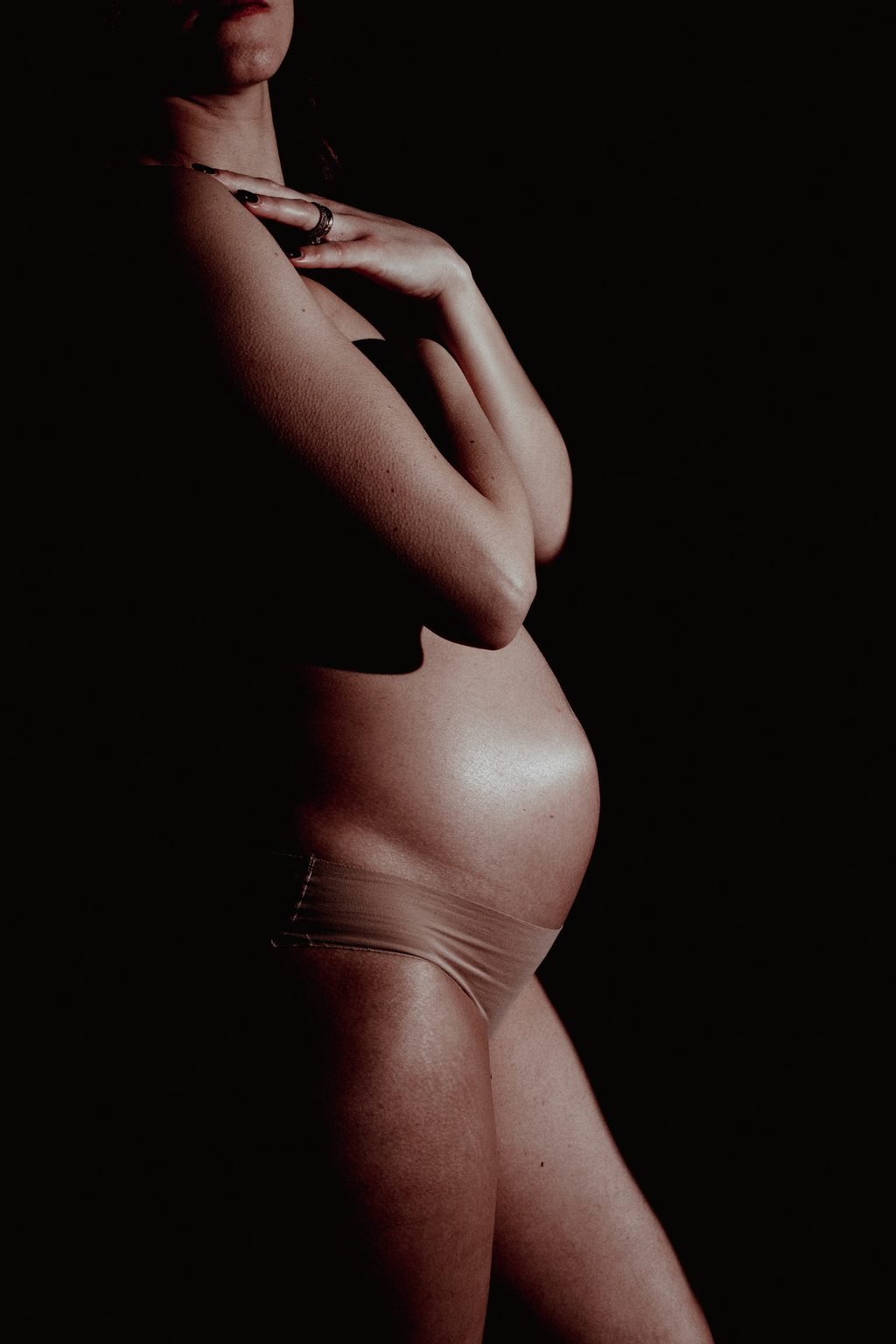 Su fondo nero, il profilo di una donna incinta illuminato da una luce laterale, con una mano sul collo