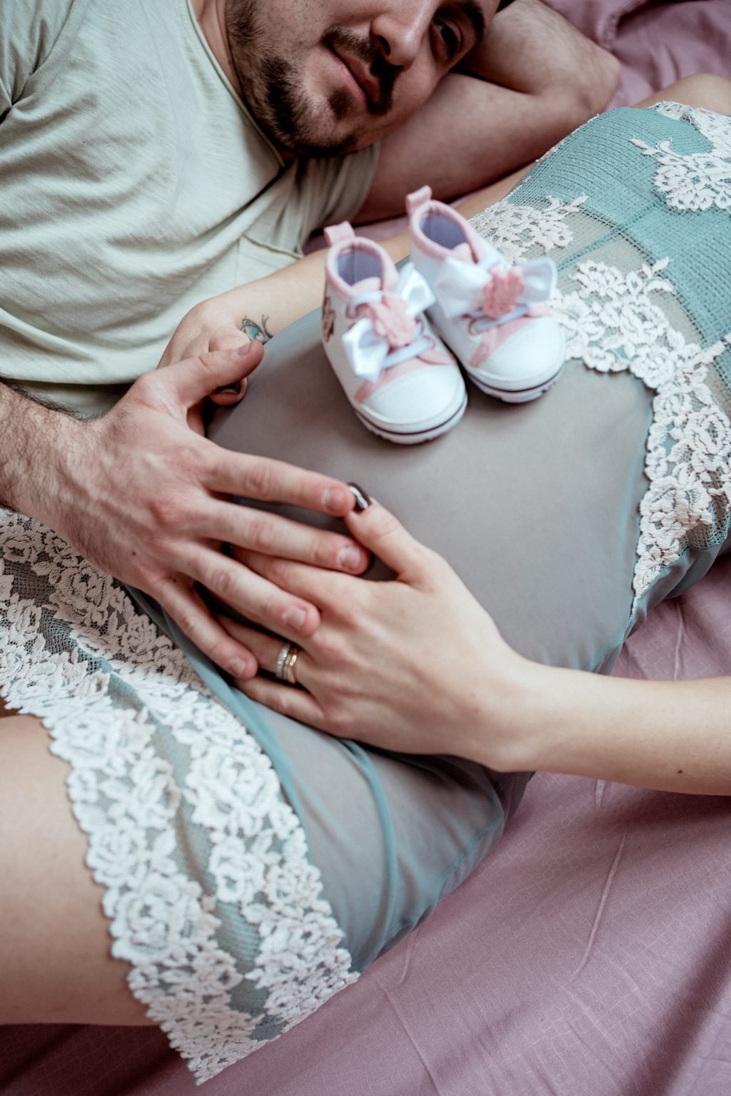 Due scarpette rosa appoggiate sulla pancia, fra le mani di lei e di lui, sul letto
