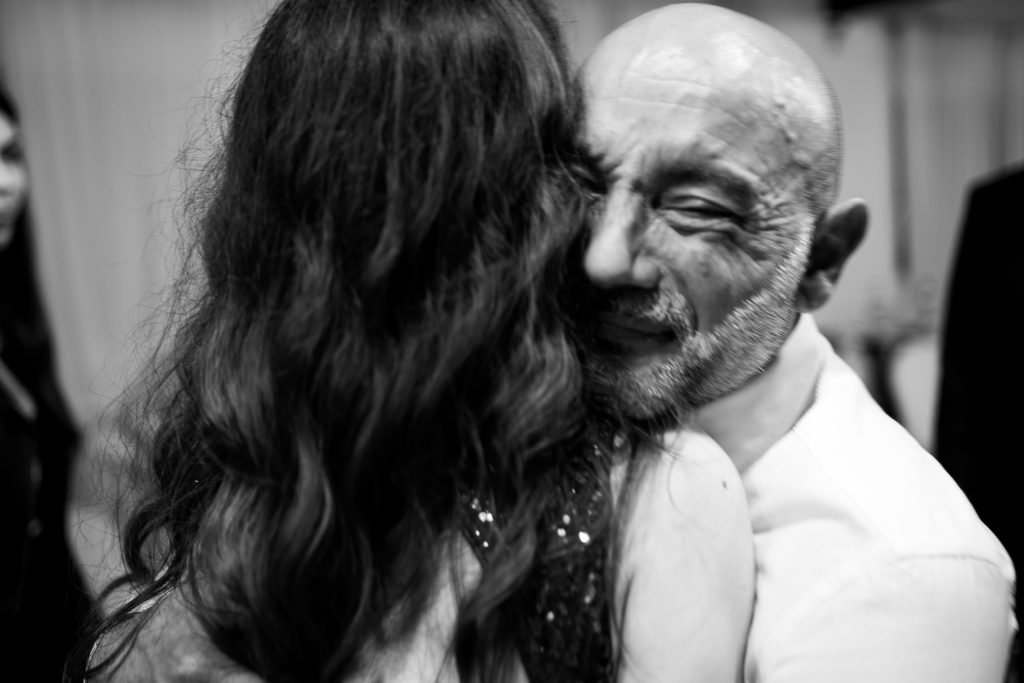 In bianco e nero, un signore anziano abbraccia la festeggiata a occhi chiusi