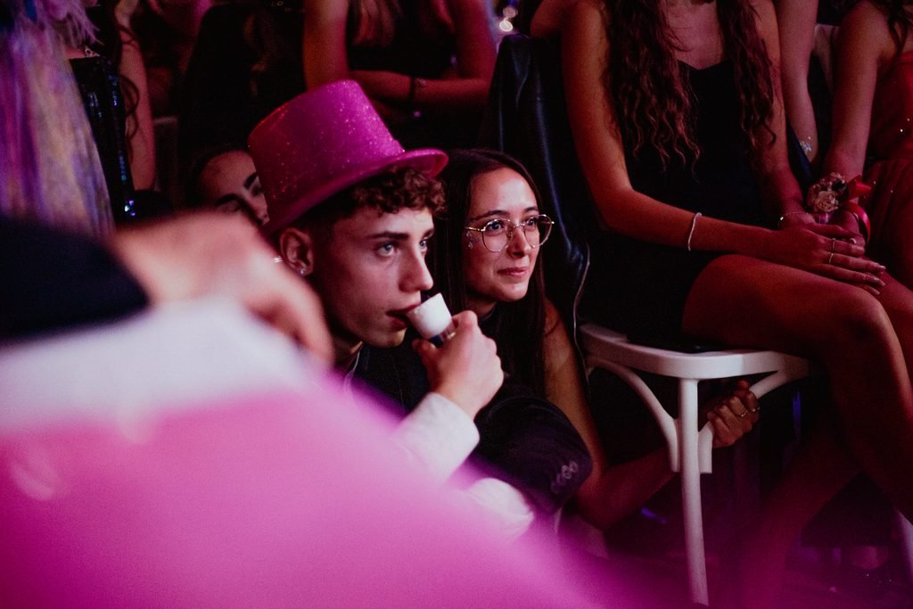 Un ragazzo con il cappello rosa di paillettes parla al microfono davanti alle amiche
