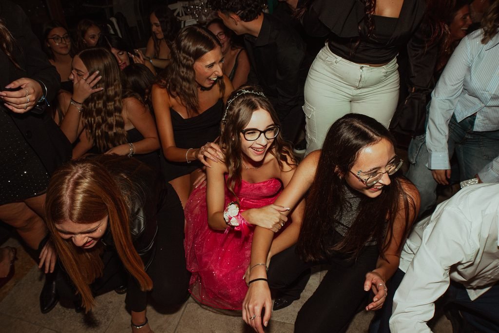 La festeggiata in abito rosa accovacciata in pista in mezzo alle amiche, tutte che ridono