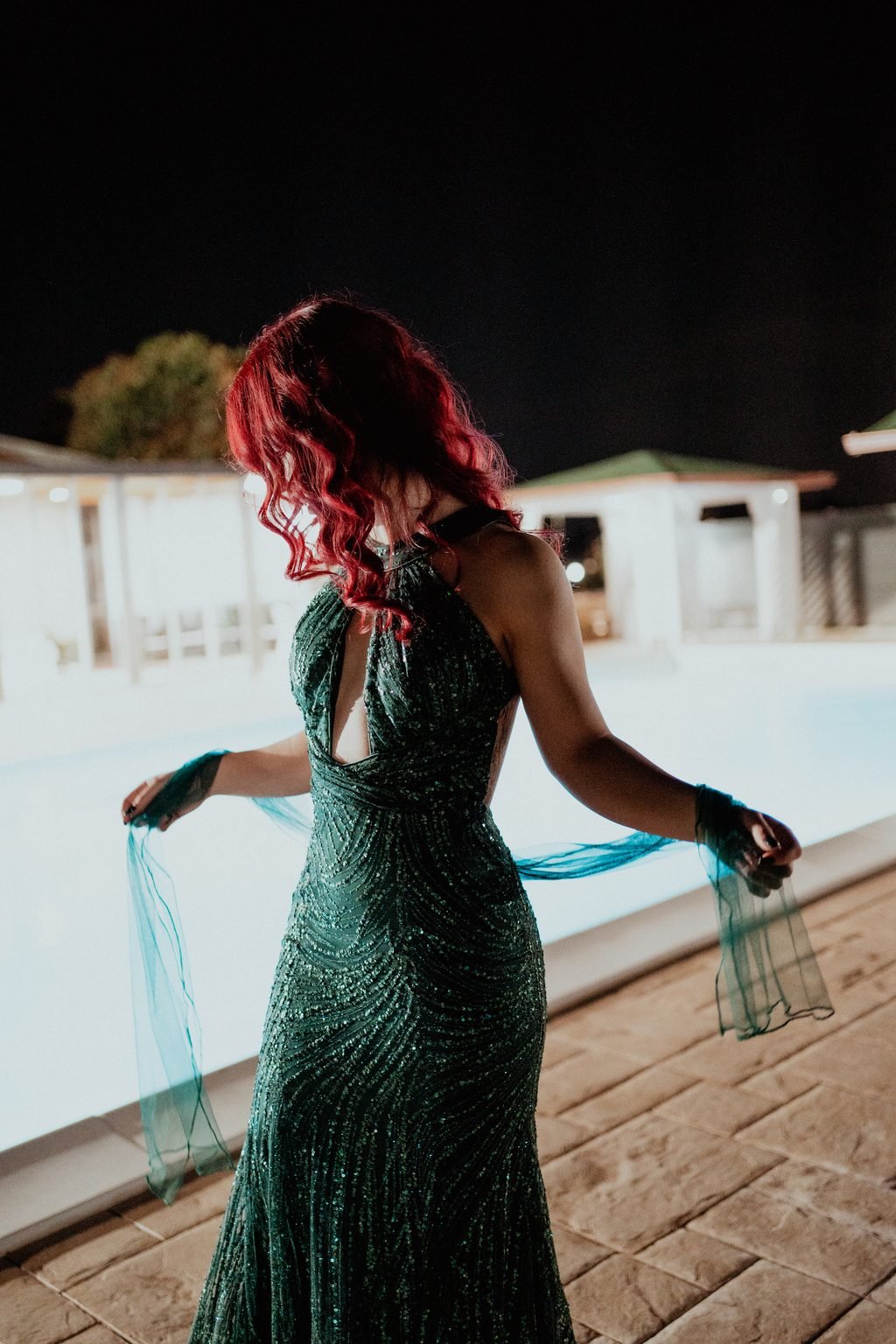 La festeggiata con i capelli rossi e l’abito verde lungo, a bordo piscina di sera, gioca con il velo