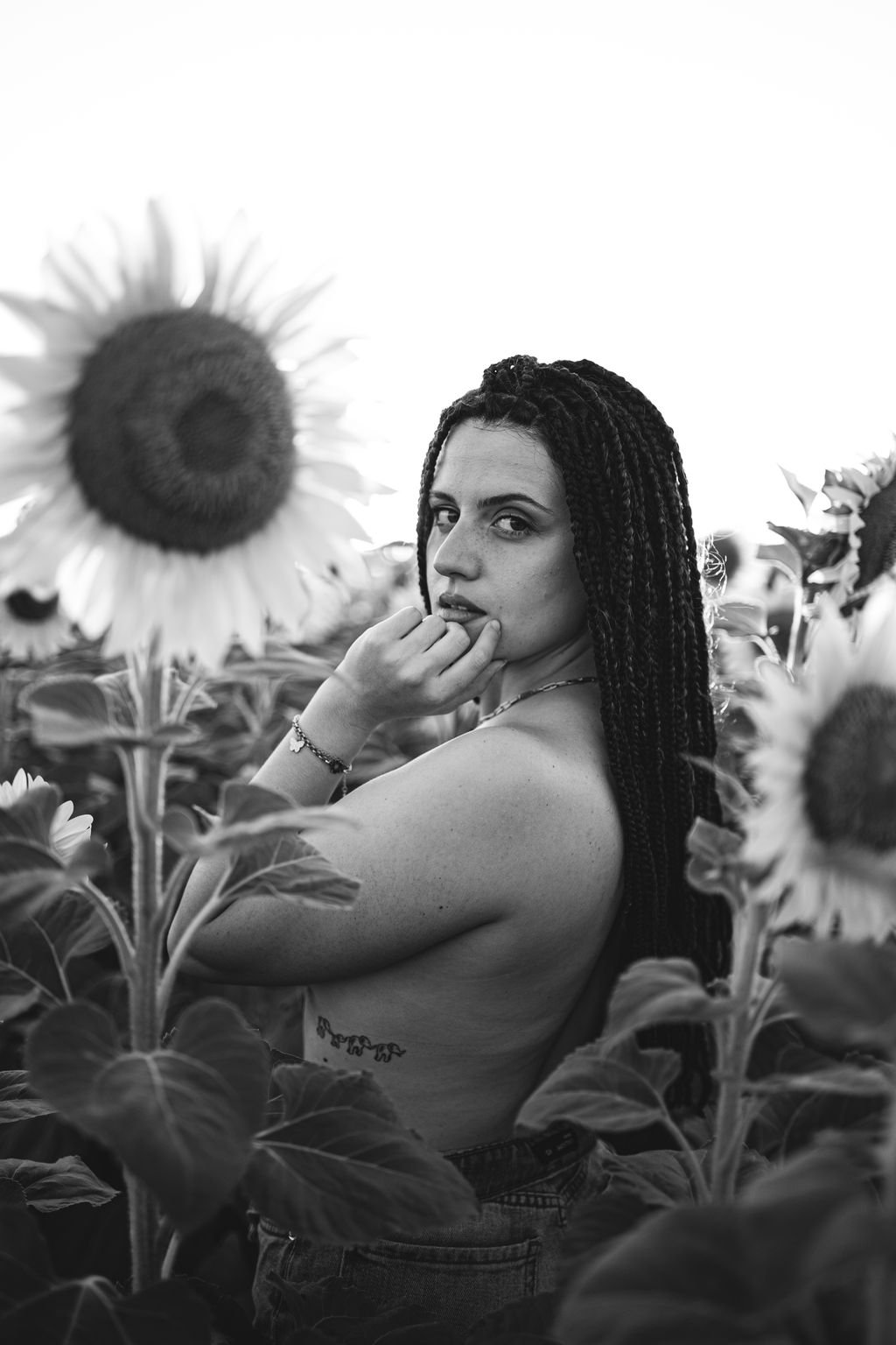 Ritratto in bianco e nero di Nemi che guarda in macchina, con la mano vicino al viso e i girasoli attorno