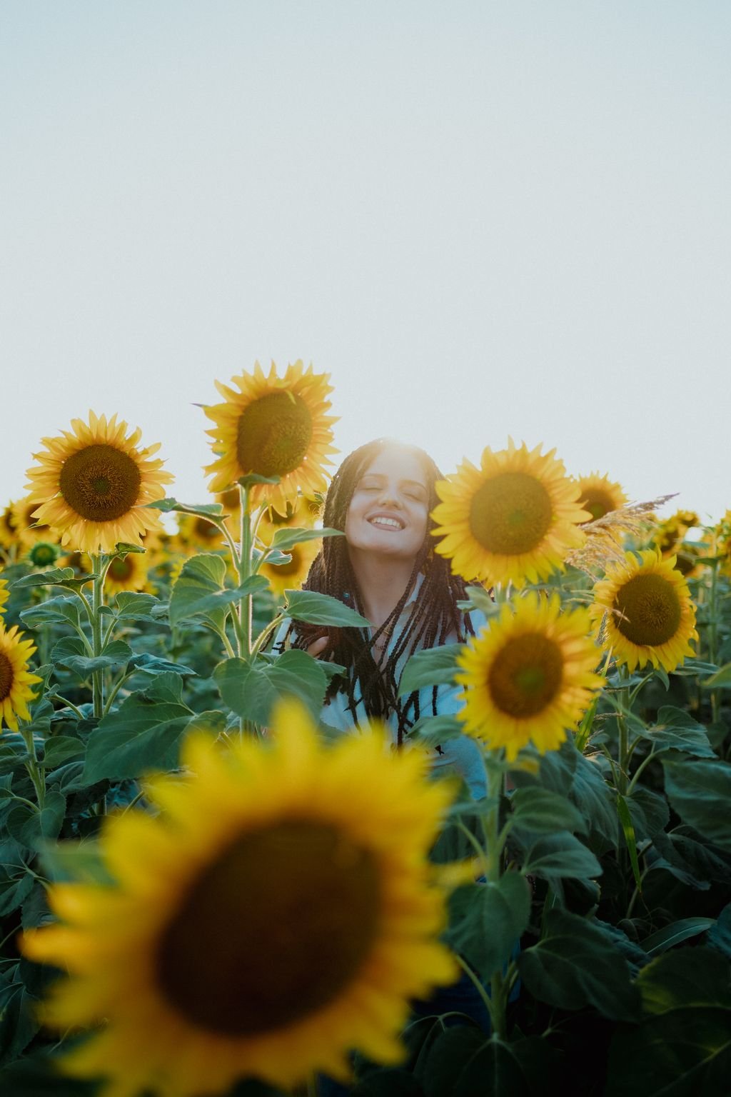 Nemi sorride a occhi chiusi fra i girasoli, con il sole che le illumina il viso