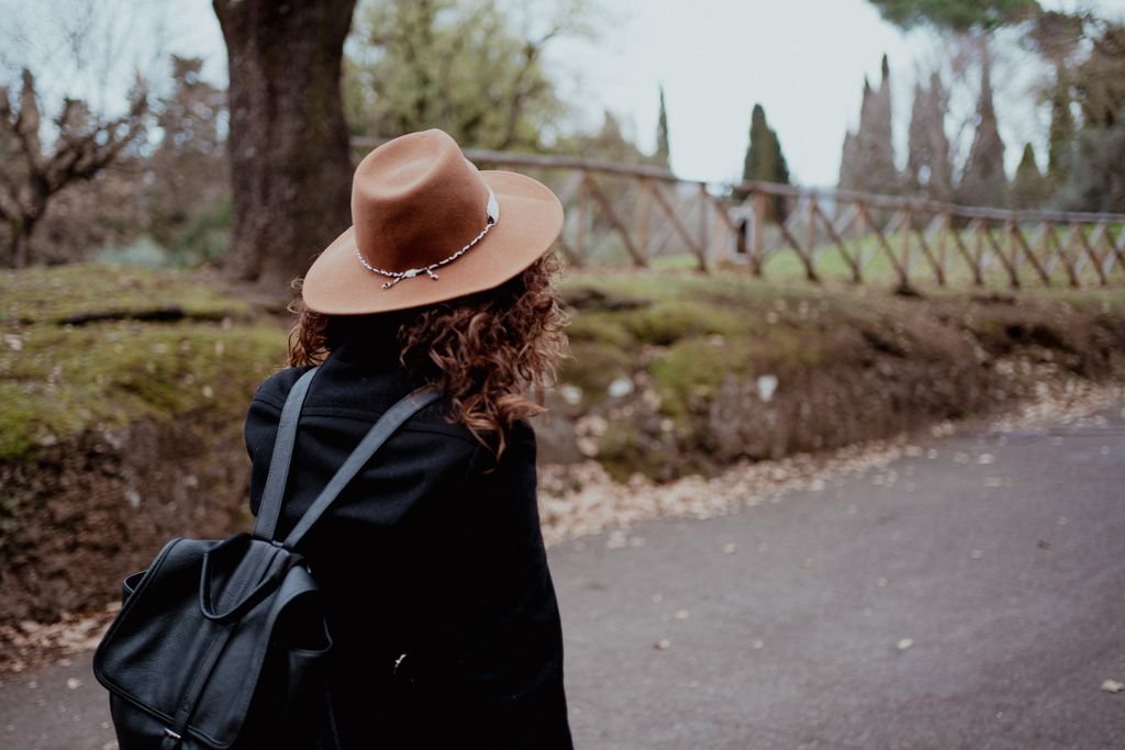 Nemi di spalle con il cappello e lo zaino, si volta a guardare il viale alberato