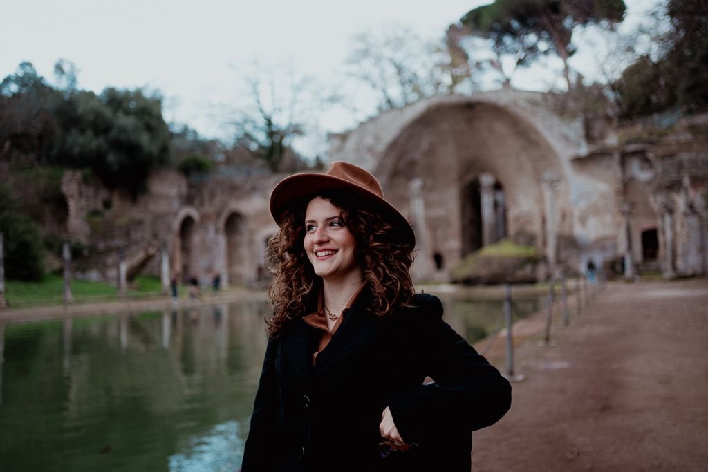 Nemi sorride con il cappello color cuoio lungo la vasca del Canopo, a Villa Adriana, con le rovine alle spalle