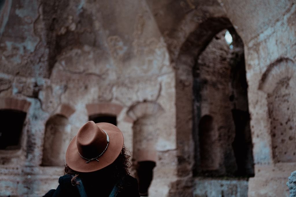 Il cappello color cuoio di Nemi davanti a una parete antica piena di nicchie ad arco