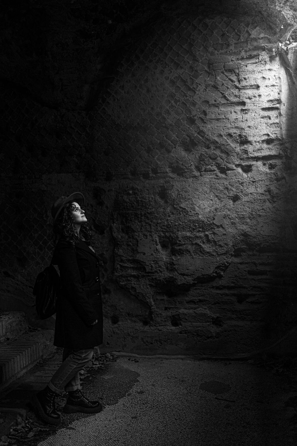 Nemi in penombra dentro una sala antica, con il viso rivolto alla luce che entra dall’alto