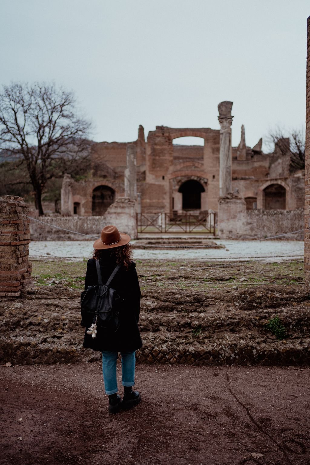 Nemi di spalle cammina verso le rovine, fra i resti di due muri antichi